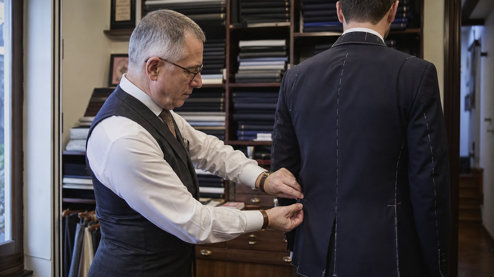 Tailleur épinglant la taille d'un pantalon de costume sur un client debout à l'atelier